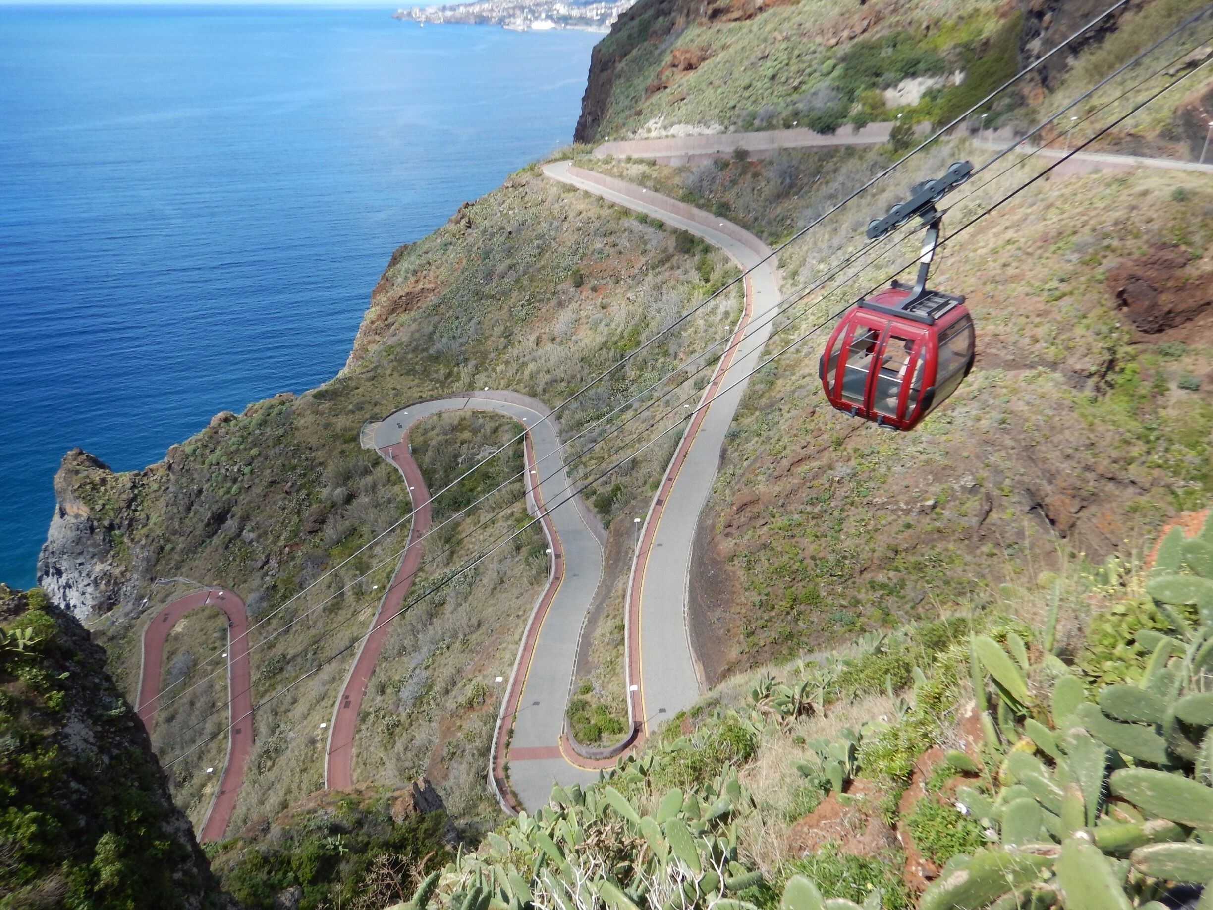 A cable car system winding along a mountainous road with a coastal view.