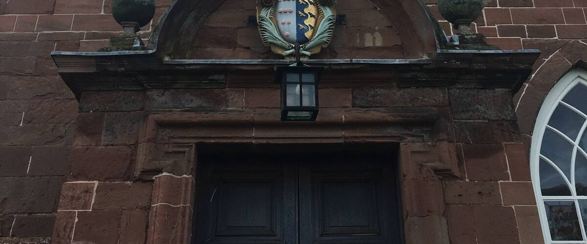 A historic building with a clock tower, a coat of arms, and a large wooden door.