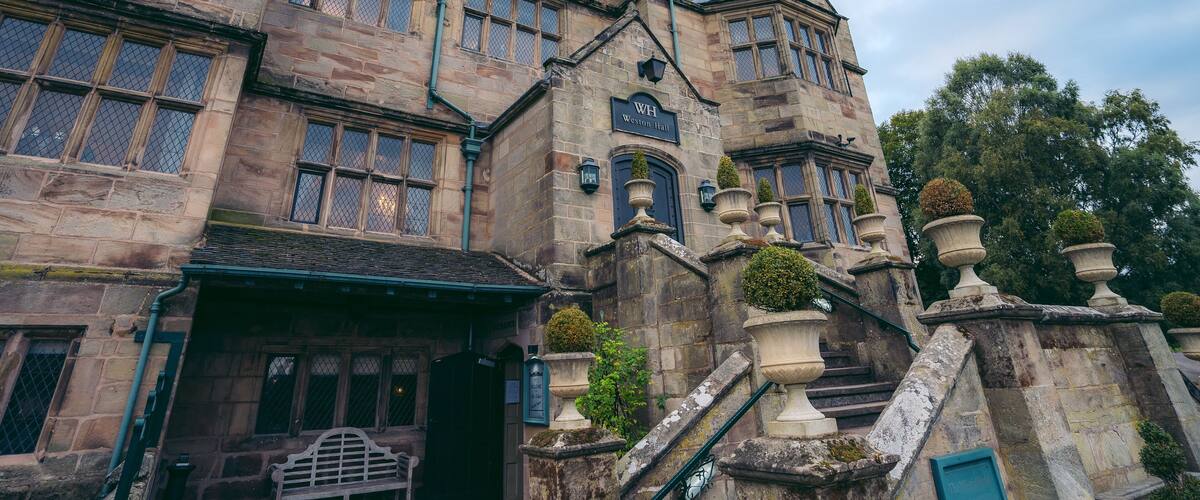 A historic stone building with multiple windows, a sign reading "Westminster Hall," and a staircase with decorative urns.