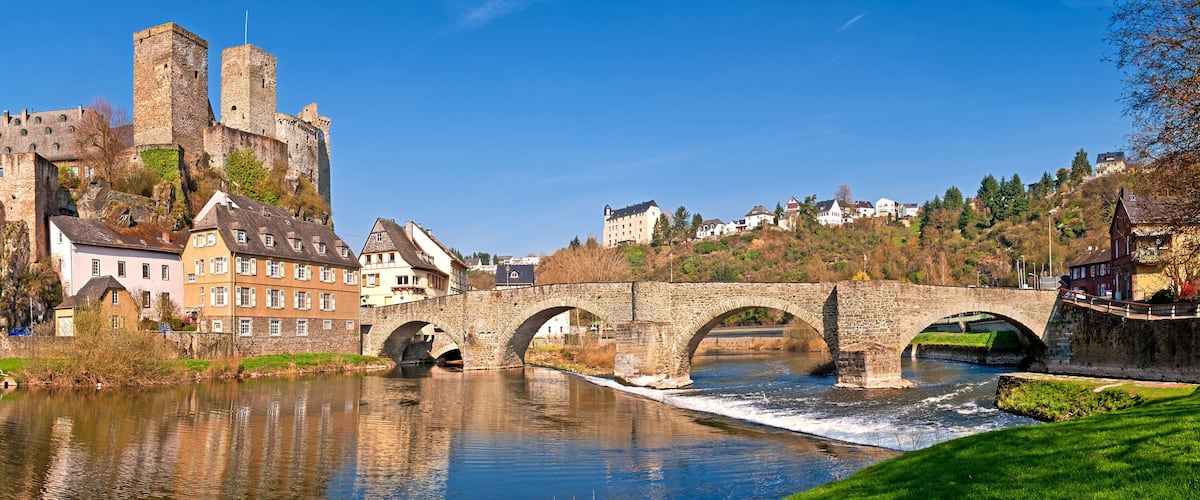 A historic stone bridge over a river, a castle on a hill, and surrounding residential buildings.