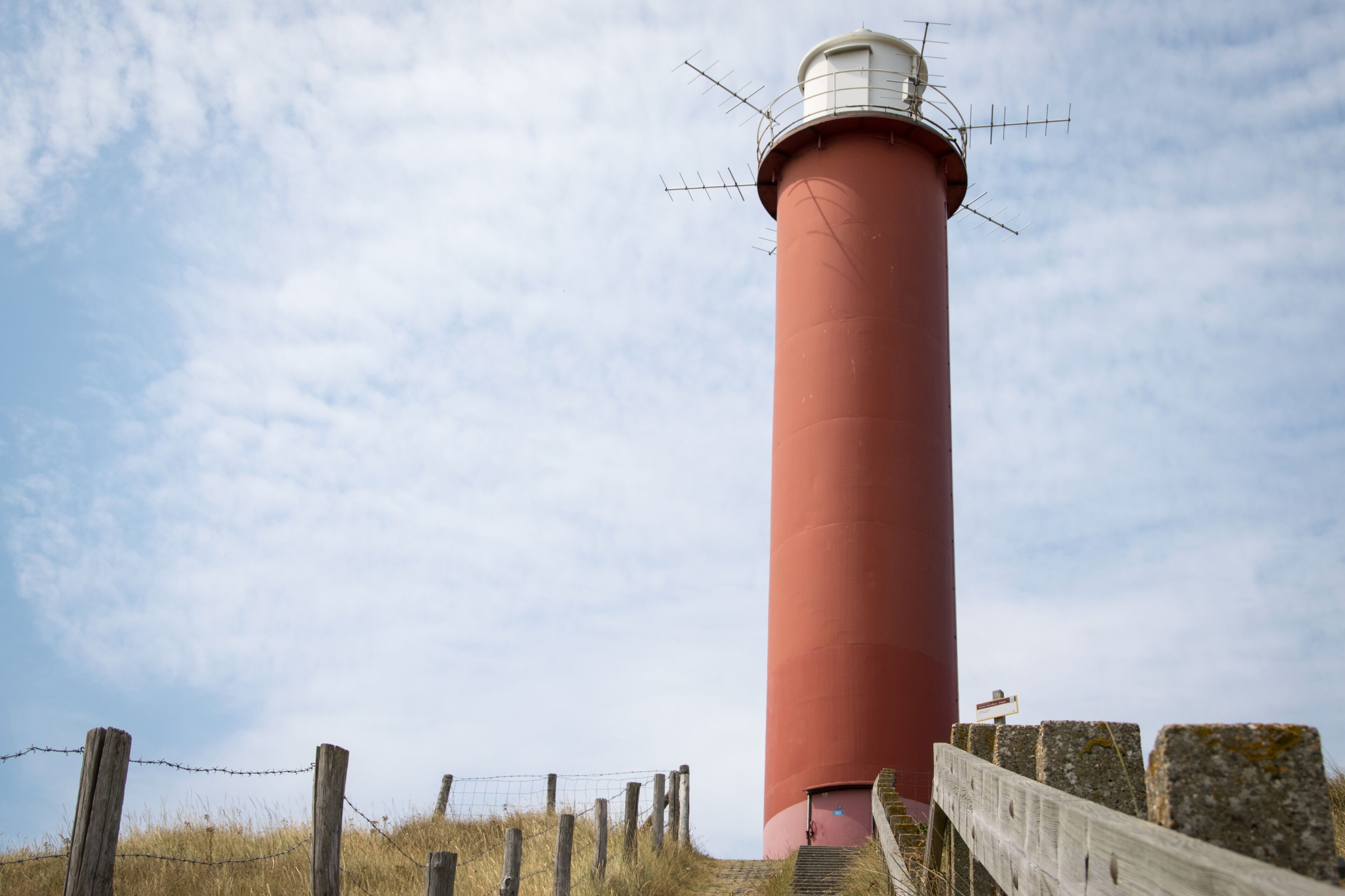 A tall red lighthouse with a white top, surrounded by a wooden fence and stone walls.