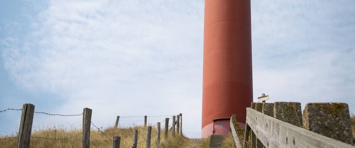 A tall red lighthouse with a white top, surrounded by a wooden fence and stone walls.