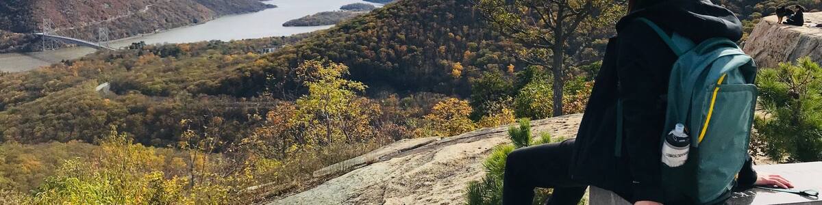 A person sitting on a concrete bench overlooking a river and hills.