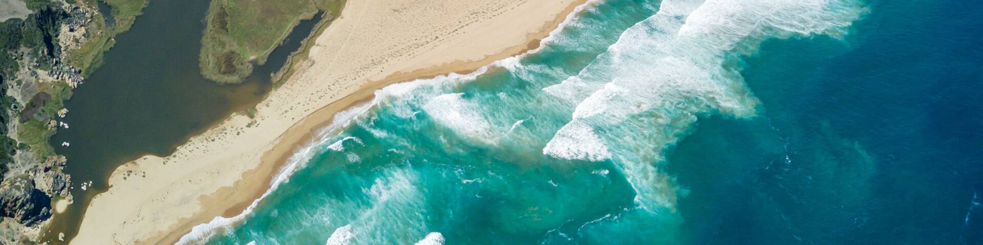 A coastal landscape with a sandy beach, a river flowing into the sea, and rocky terrain.