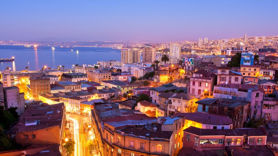 A cityscape at dusk with illuminated buildings and a river in the background.