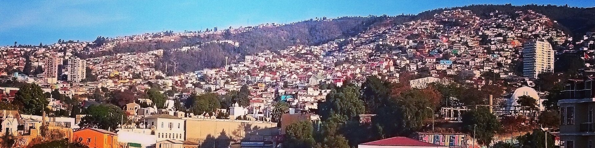 Un paisaje urbano con una zona residencial muy poblada, una colina destacada al fondo y un cielo azul despejado.