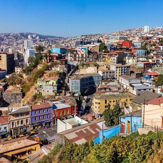 A densely packed urban area with colorful buildings and a hillside in the background.