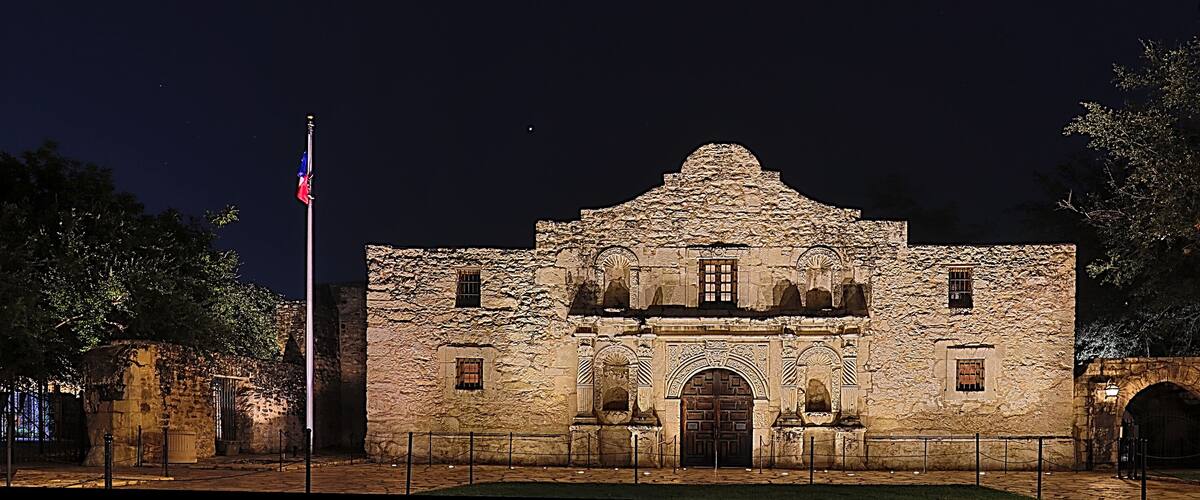 A historic stone building with a prominent entrance and arched windows, illuminated at night.