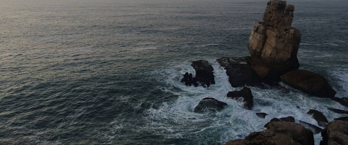 A coastal landscape with a prominent rock formation and waves crashing against it.