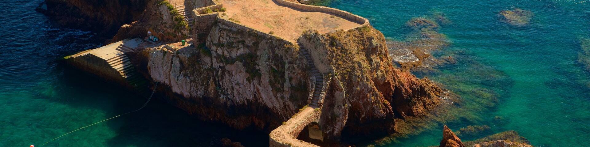 A coastal fortress with a large tower, a staircase leading up to the entrance, and a boat in the water.