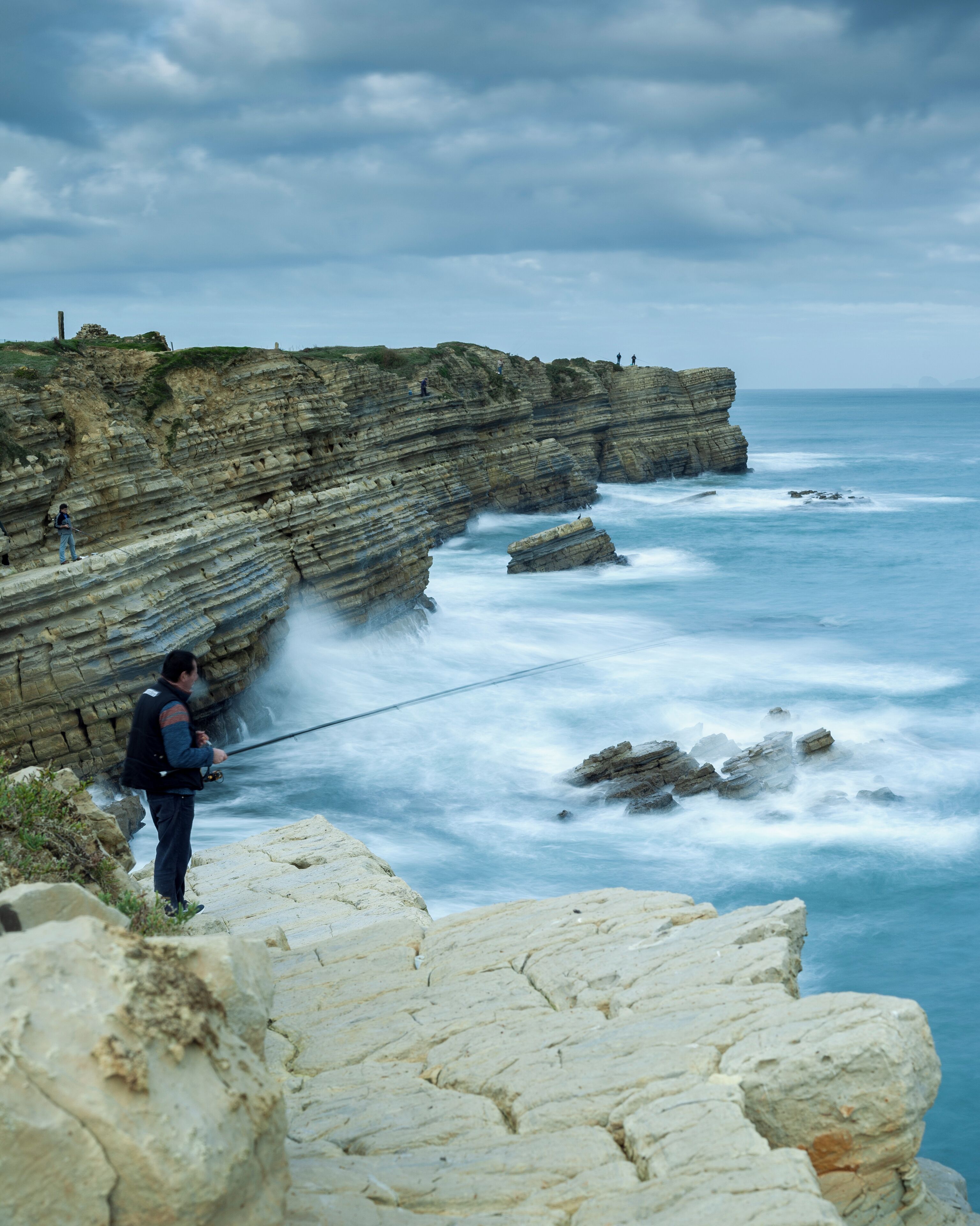 A rocky coastline with layered cliffs and a person fishing.