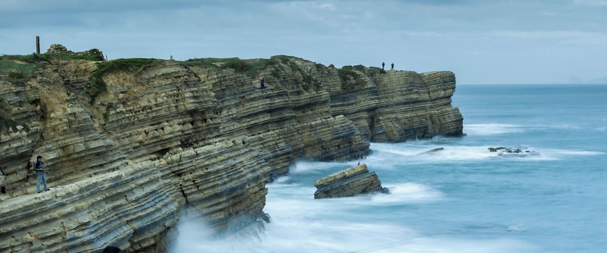 A rocky coastline with layered cliffs and a person fishing.