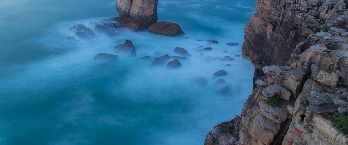 A coastal rock formation with a prominent pillar-like structure surrounded by smaller rocks and a vast ocean.