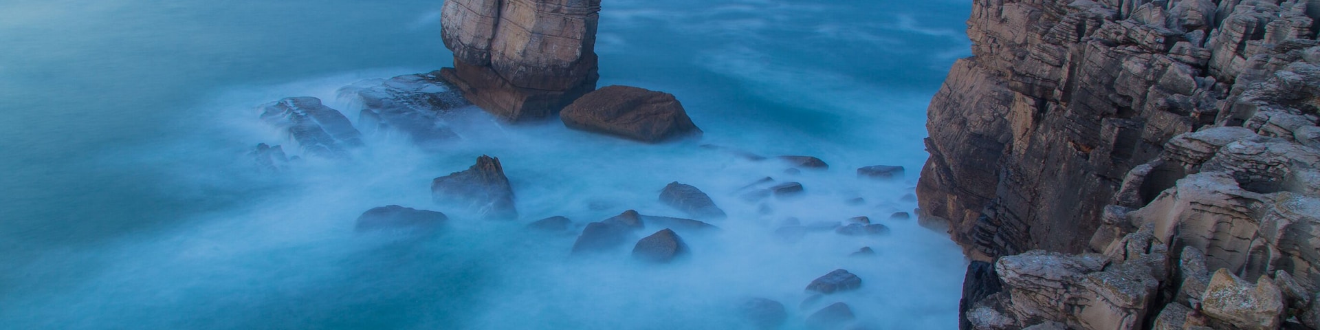 A coastal rock formation with a prominent pillar-like structure surrounded by smaller rocks and a vast ocean.