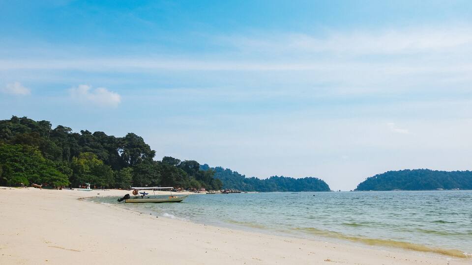 A beach with a boat, calm water, and forested hills in the background.