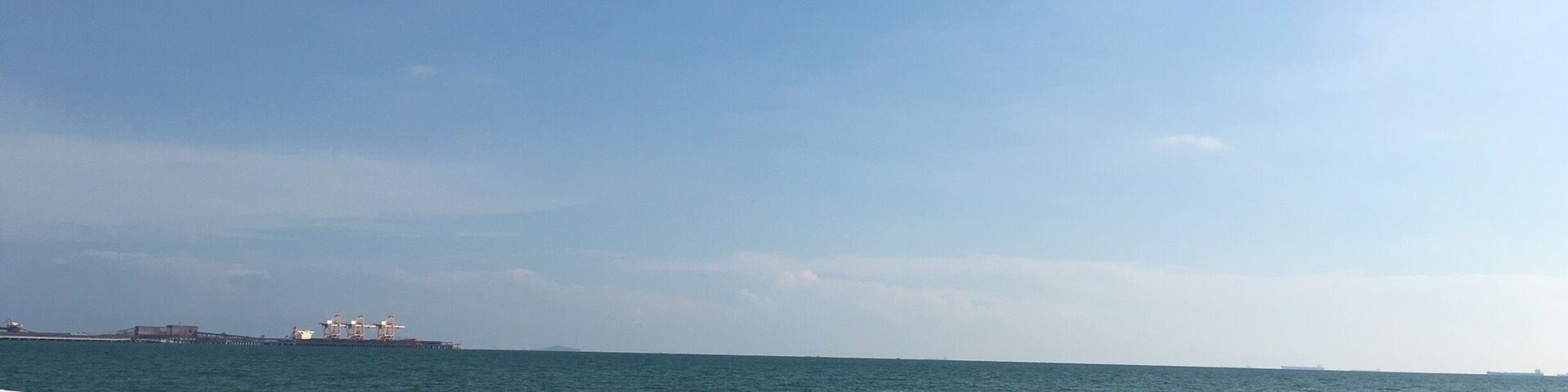 Una playa con gente nadando y caminando sobre la arena, un muelle al fondo y un cielo despejado.