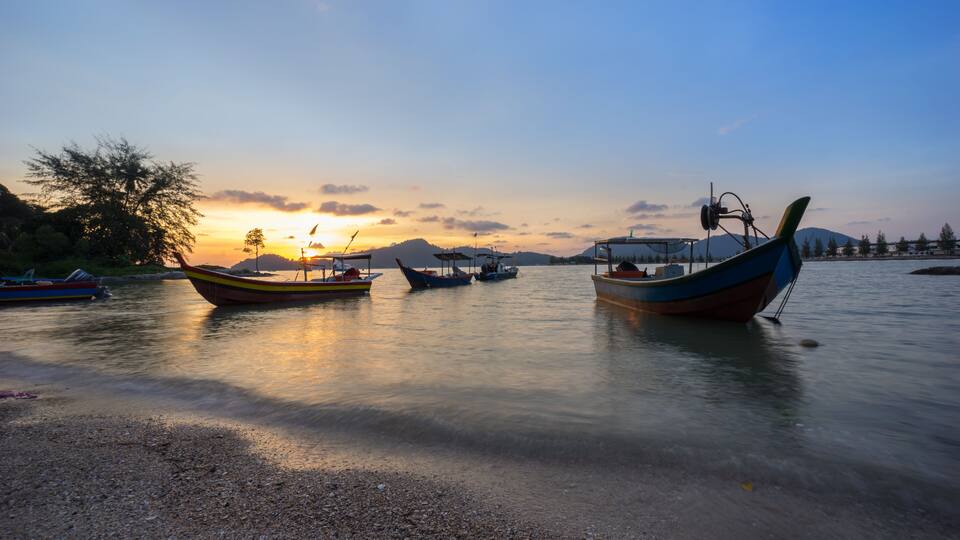 A calm lake at sunset with several boats anchored near the shore.