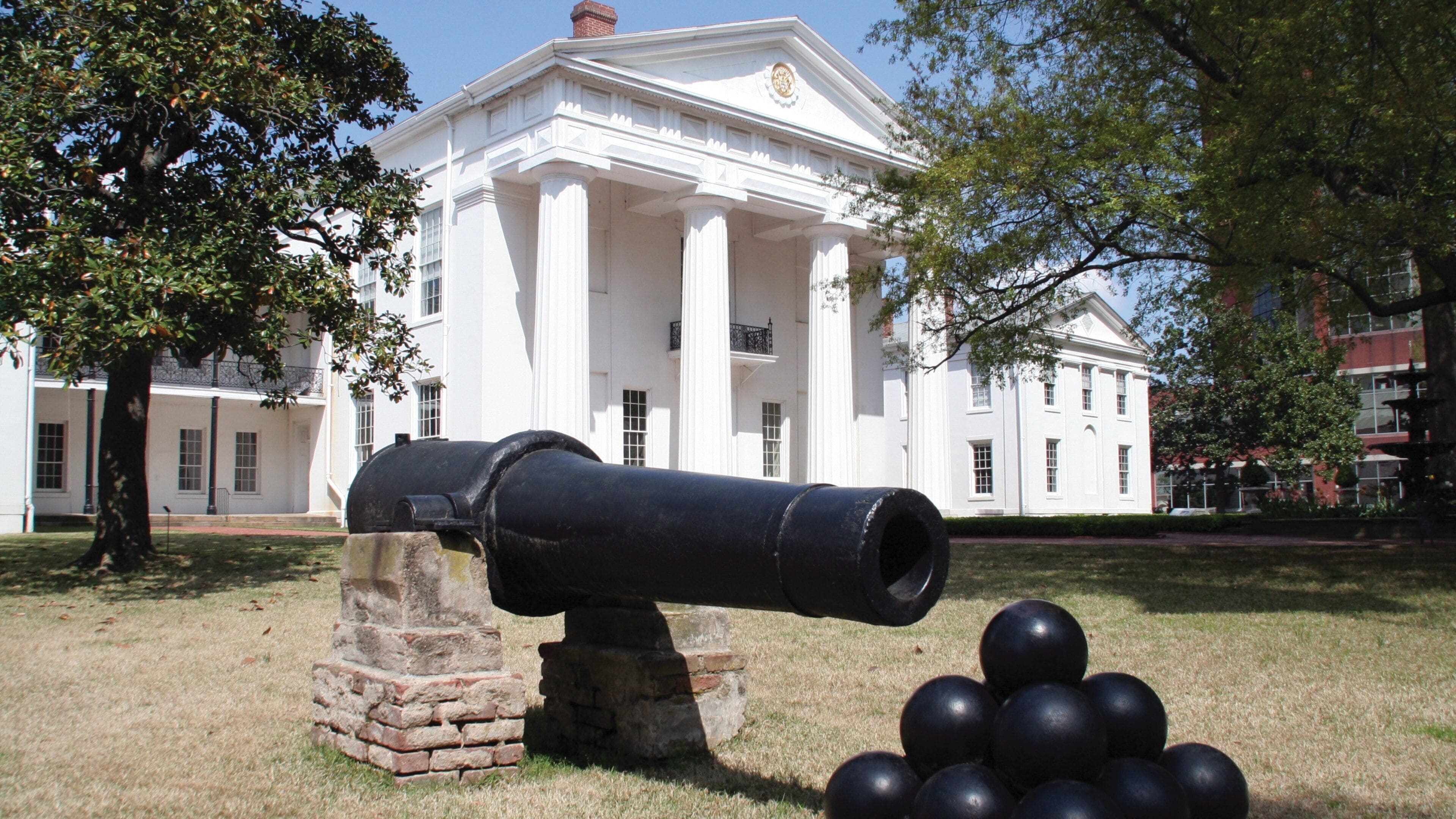 A cannon in front of a white building with columns.