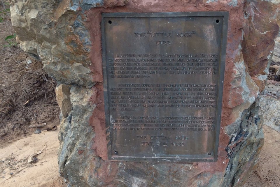 A weathered plaque on a rock with historical text.