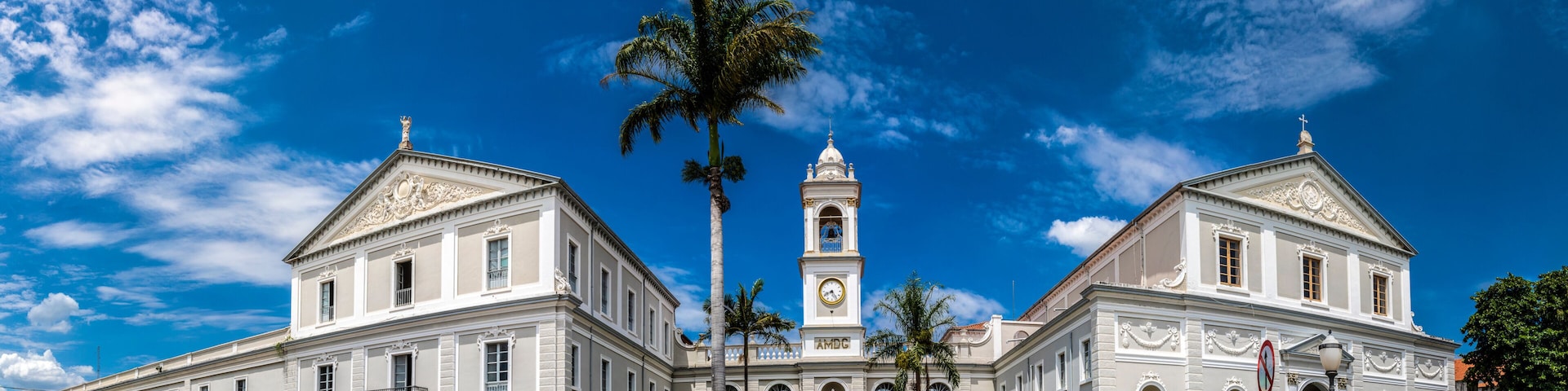A historic building with two towers, a clock, and a palm tree.
