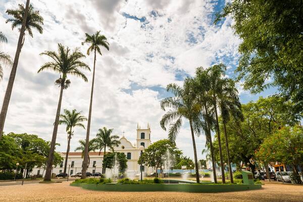 Uma igreja histórica rodeada por palmeiras e uma fonte.