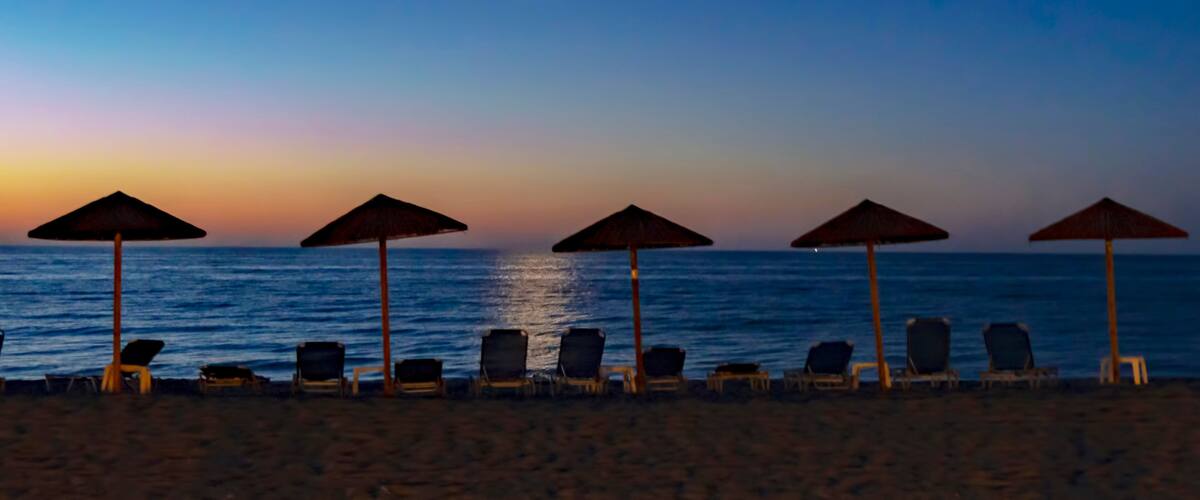A beach at sunset with umbrellas and lounge chairs.