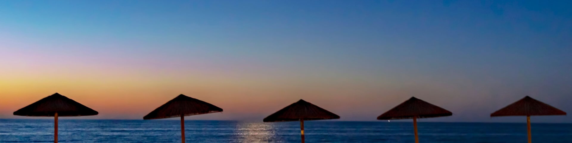 A beach at sunset with umbrellas and lounge chairs.