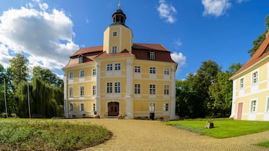Ein gelbes Gebäude mit rotem Dach, einem Turm und einem Garten mit Bänken.