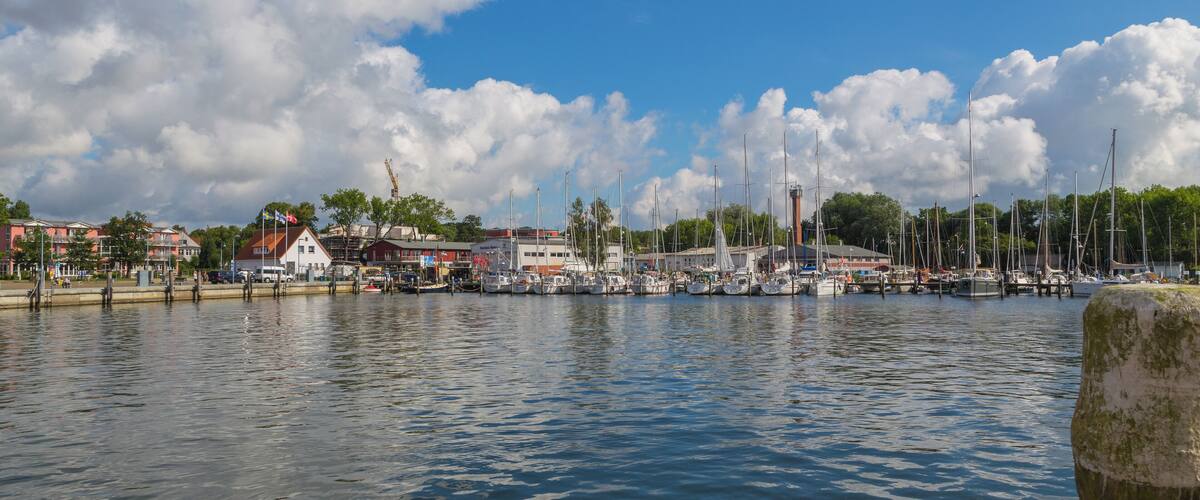 A marina with boats docked, buildings, and a clear sky.