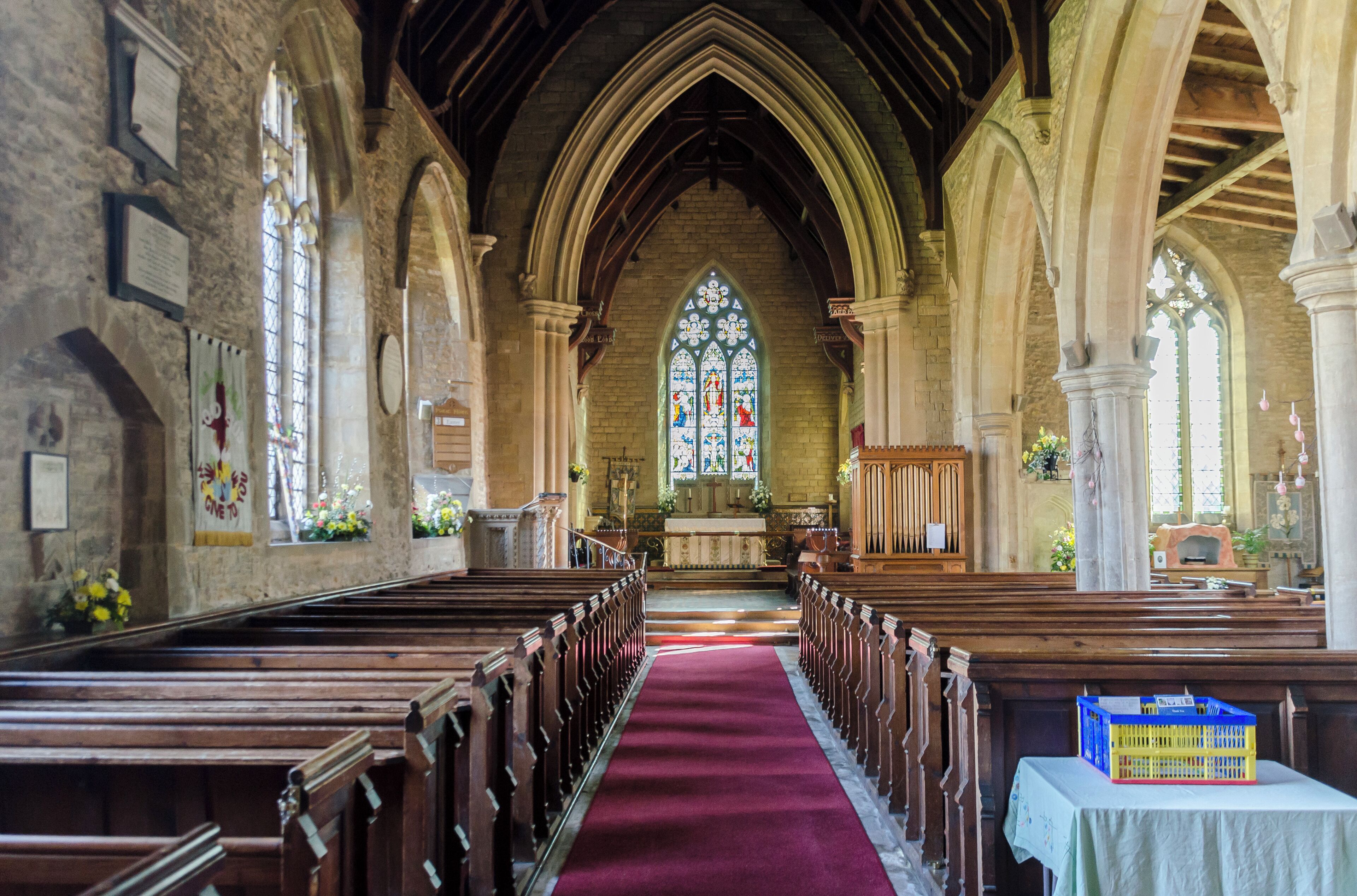 Late 12th C onwards and chancel rebuilt in 1863. 3 stage tower, the lower part is built of small rubble-work with an ashlar framework and buttresses. The west door is late 12th century with two orders of shafts, waterleaf capitals and a round moulded arch. The belfry contains four bells which can no longer be rung due to cracking in the tower and the need for extensive renovations and a new bell frame. The 14th broach spire is a fine example which carries three tiers of lucarnes and is ornamented with grotesques, which perch menacingly as if ready to leap down. The top 3 metres of the spire was renewed in 1909 and the weathercock added. The south porch, known as the Angel Porch, has carved stone angels on either side of the entrance and the south door is of the same date as the tower. Just inside the church is the font – the base and stem are Early English but the octagonal bowl is believed to be 16th century, judging by the costumes of the figures, but carved in an archaic crude style with biblical and symbolic figures,the underside of the bowl is also decorated with carved figures. The aisle is 13-14th century and separated from the nave by a Decorated arcade of three bays with seats at the base of the pillars which are now obscured by pews.To the left of the chancel is a blocked up doorway which may previously have led to a rood screen. In the north wall of the Nave is the old north door, known as the Devil’s Door, which is now blocked up and set into the masonry here is the carved effigy of a child. The pulpit is of Ancaster stone and replaces one that stood where the organ now stands. At the foot of the organ and to its left is a marble memorial slab to Charles Medlycot, who was murdered by an absconding servant in 1737 on the eve of his wedding.