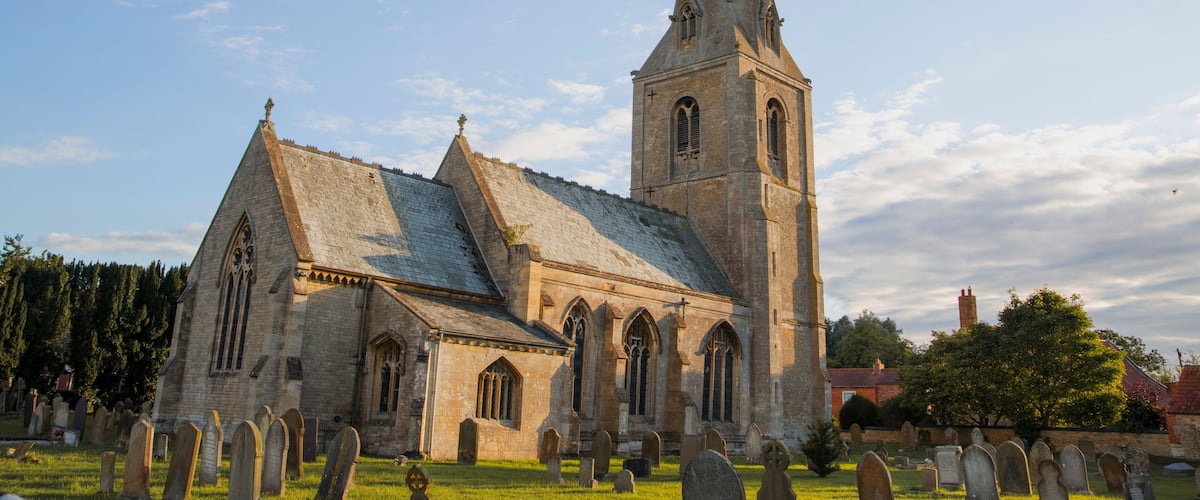 A church with a tall steeple and a graveyard in front.