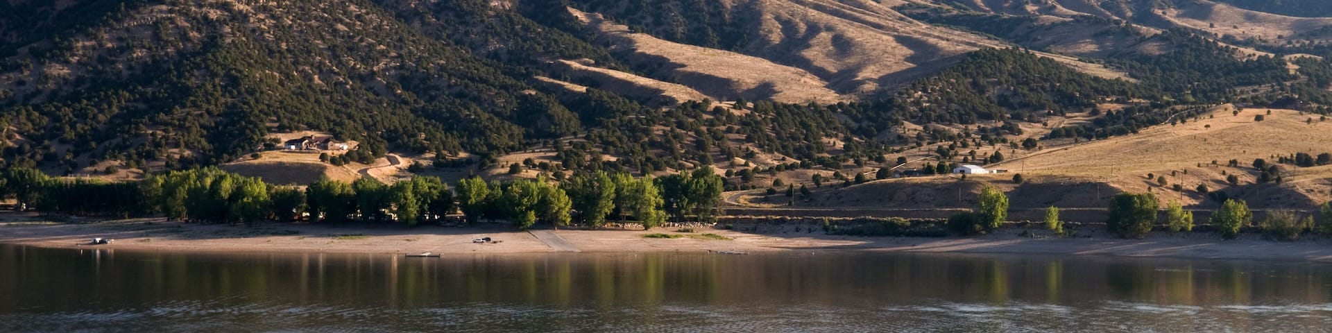 A calm lake with ripples, surrounded by rolling hills and sparse vegetation.