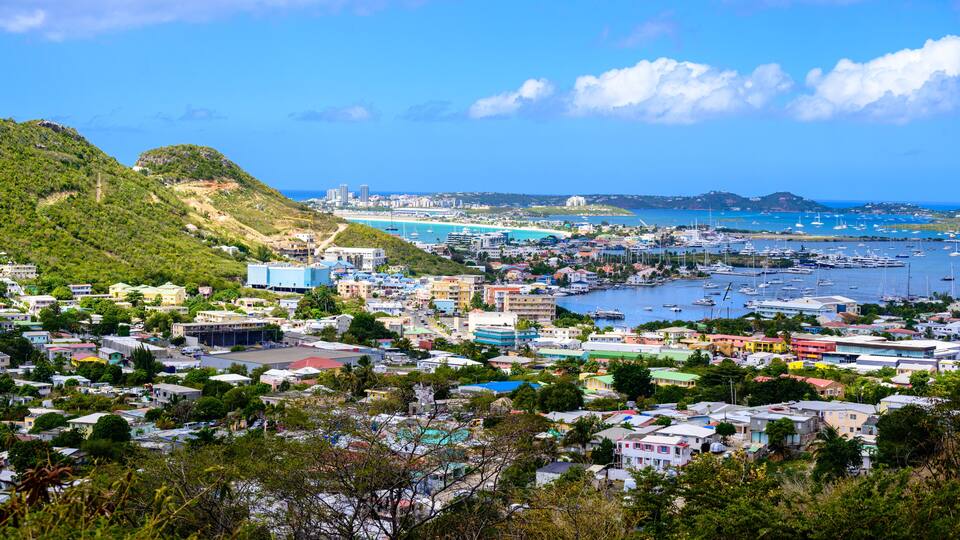 A coastal town with a marina, buildings, and hills in the background.