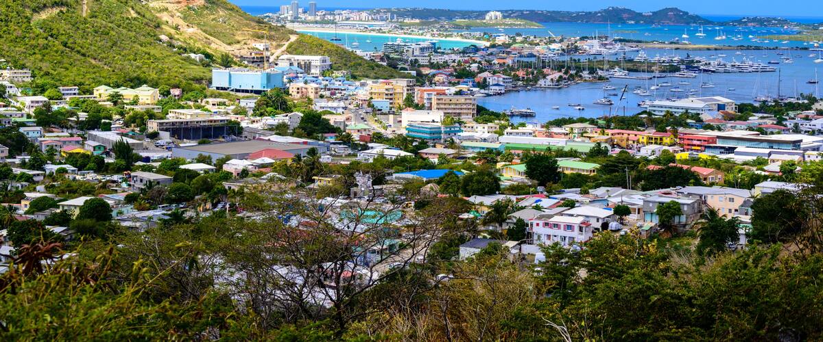 A coastal town with a marina, buildings, and hills in the background.