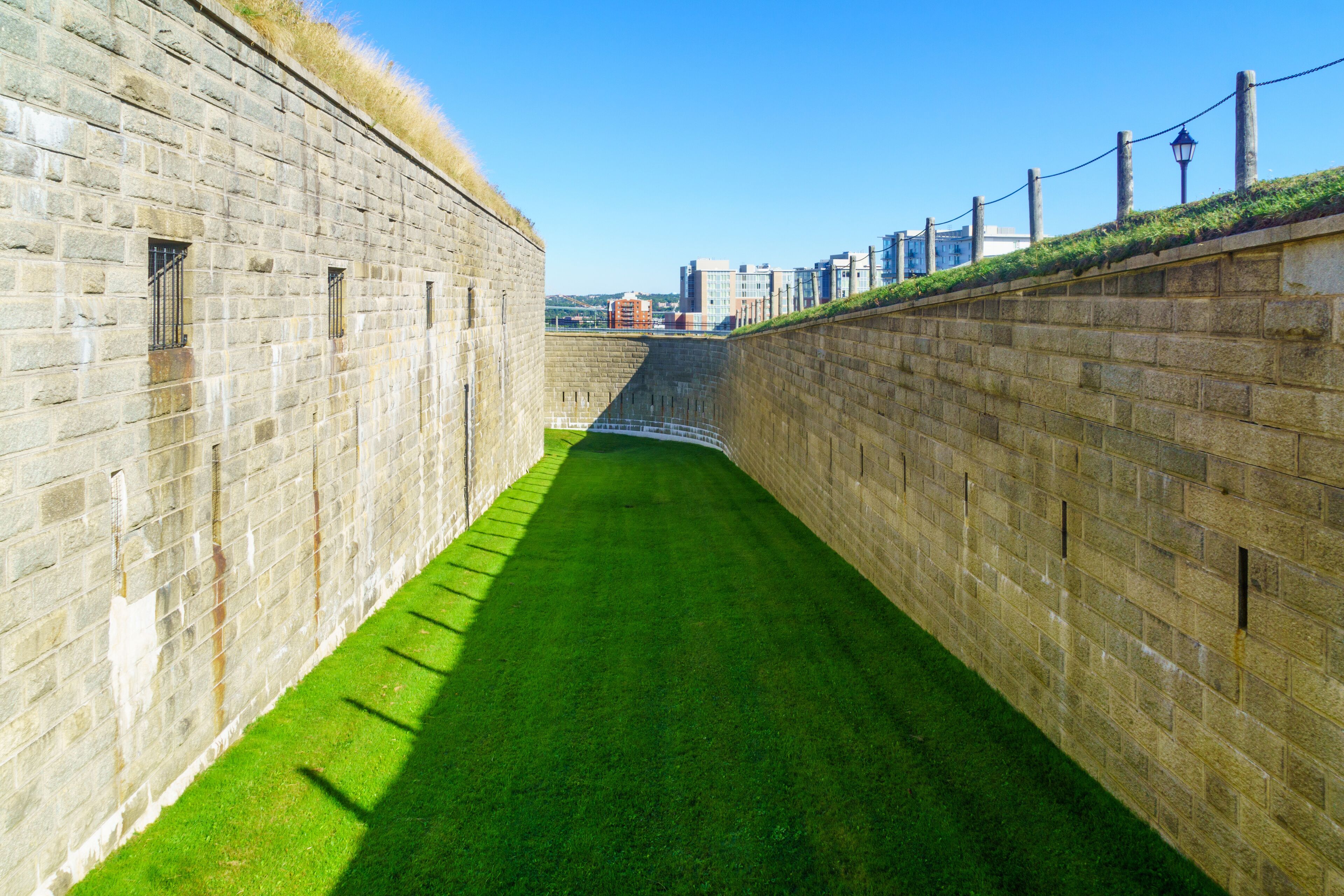 A narrow stone pathway flanked by high stone walls with a grassy area in the center.