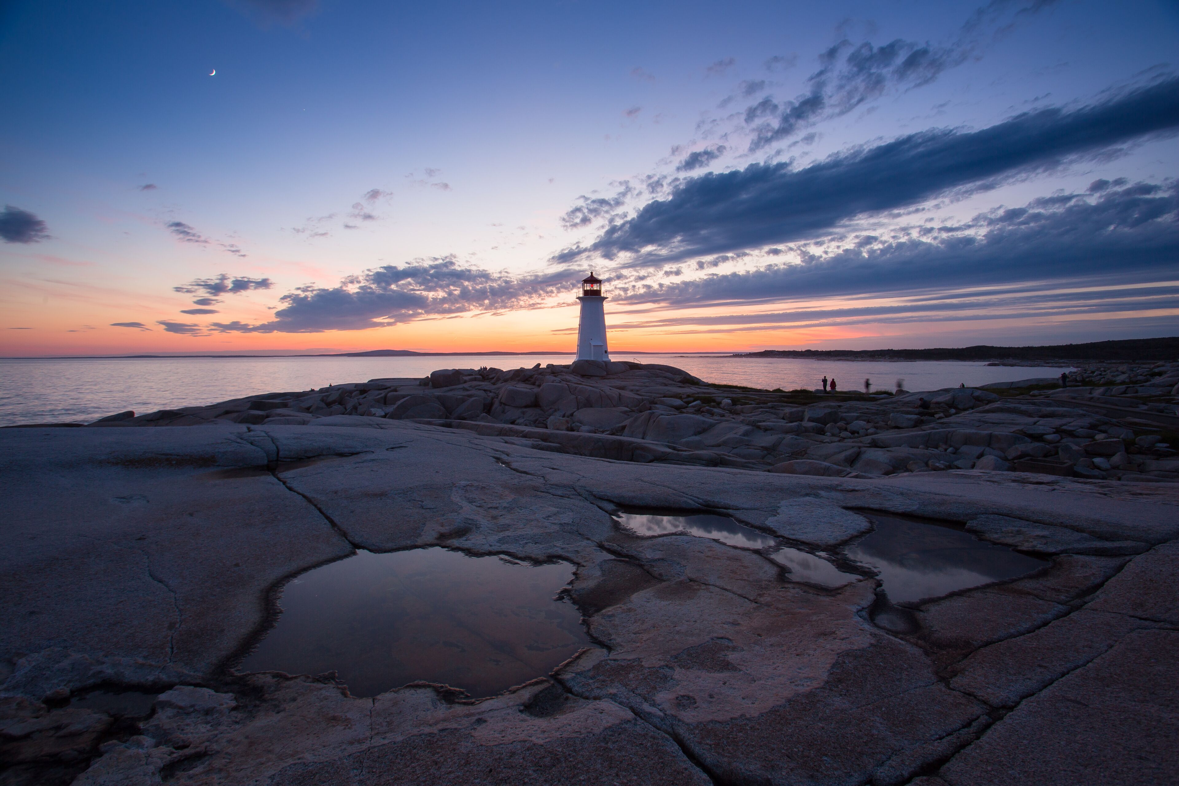 A lighthouse on a rocky shore at sunset with a clear sky.