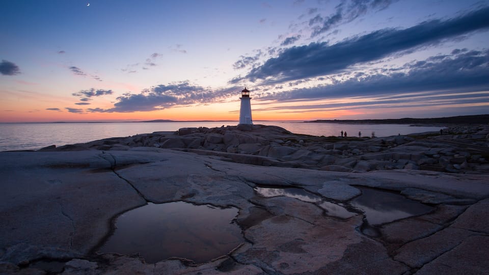 A lighthouse on a rocky shore at sunset with a clear sky.