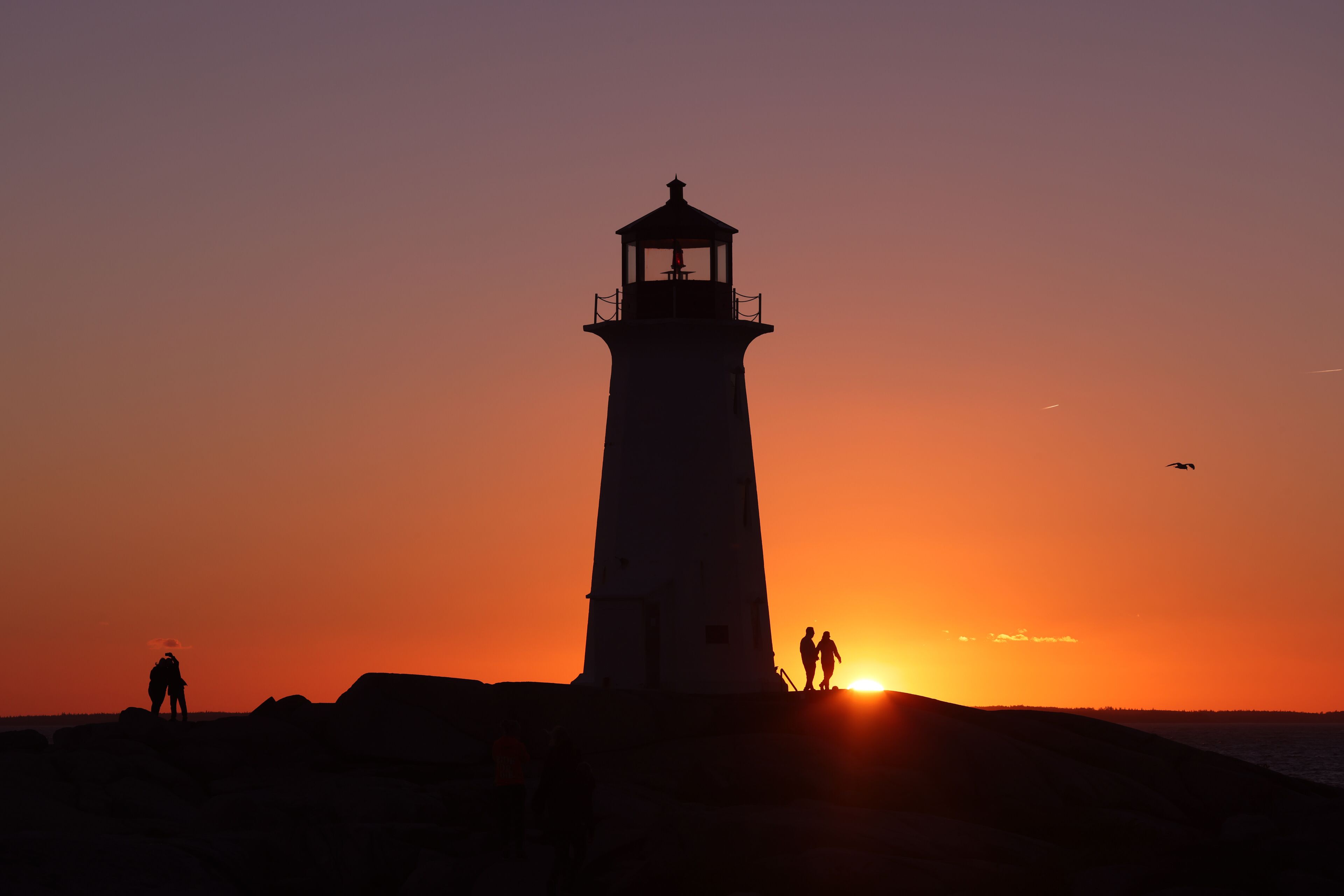 A lighthouse silhouette against a sunset sky, with two people standing at its base.