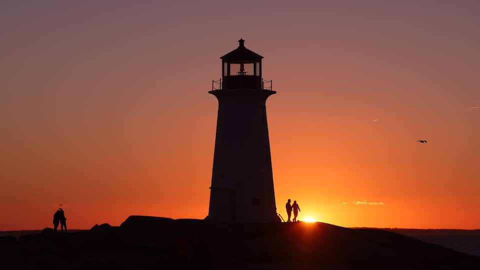 A lighthouse silhouette against a sunset sky, with two people standing at its base.