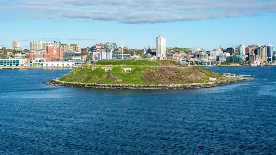 A coastal cityscape with a prominent hill with buildings on top, a large body of water, and a distant skyline of various buildings.