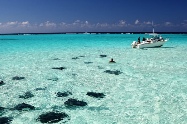 A clear turquoise sea with a boat and a person swimming.