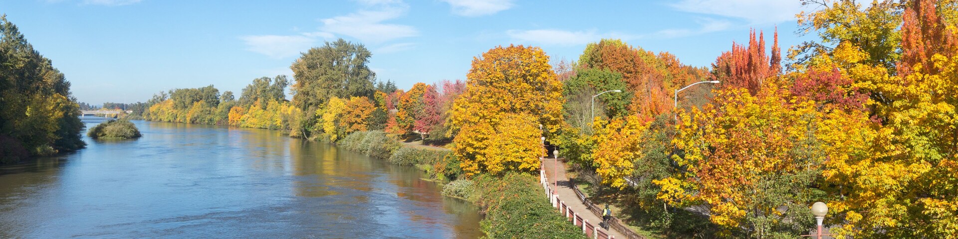 Un río con follaje otoñal, un puente y un camino para peatones.
