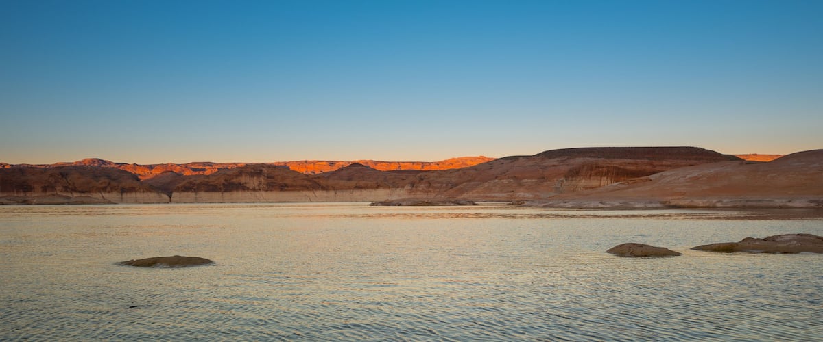 A calm lake with rocky terrain and mountains in the background.
