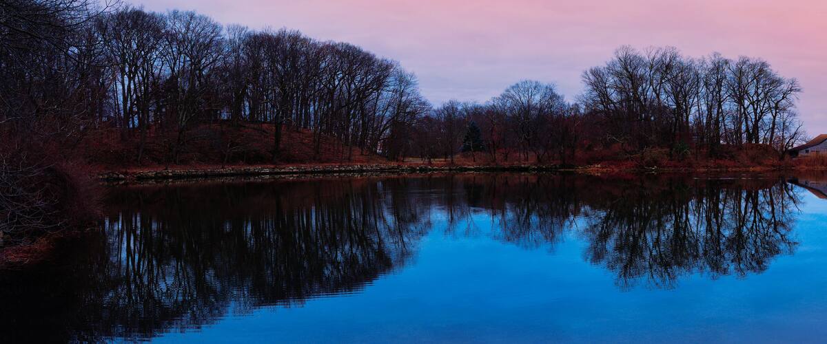 A calm river reflecting trees and a house.