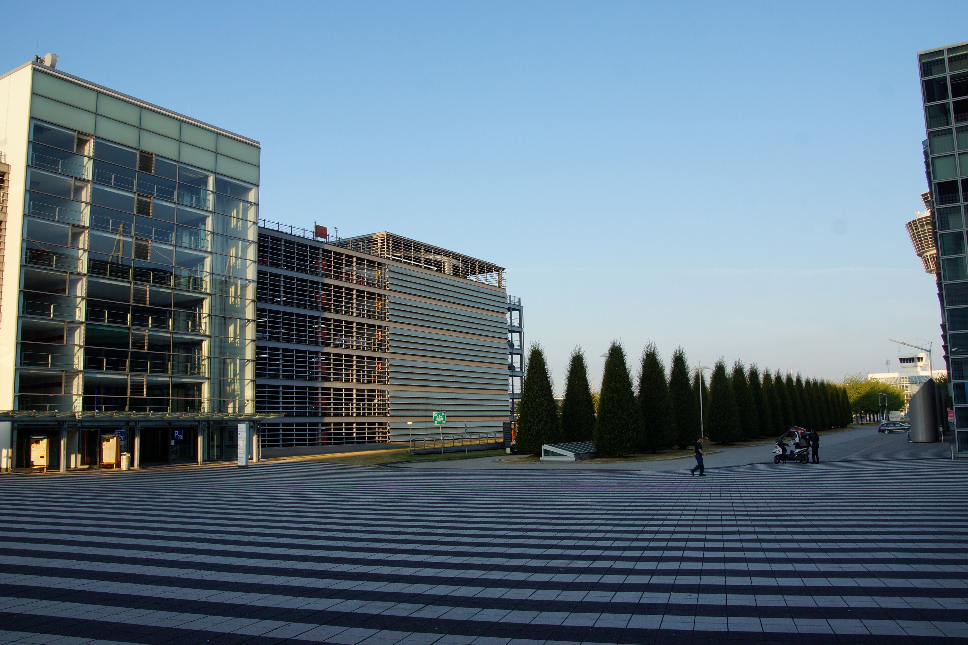 A modern urban plaza with a pedestrian crossing, a large glass building, and a construction site.