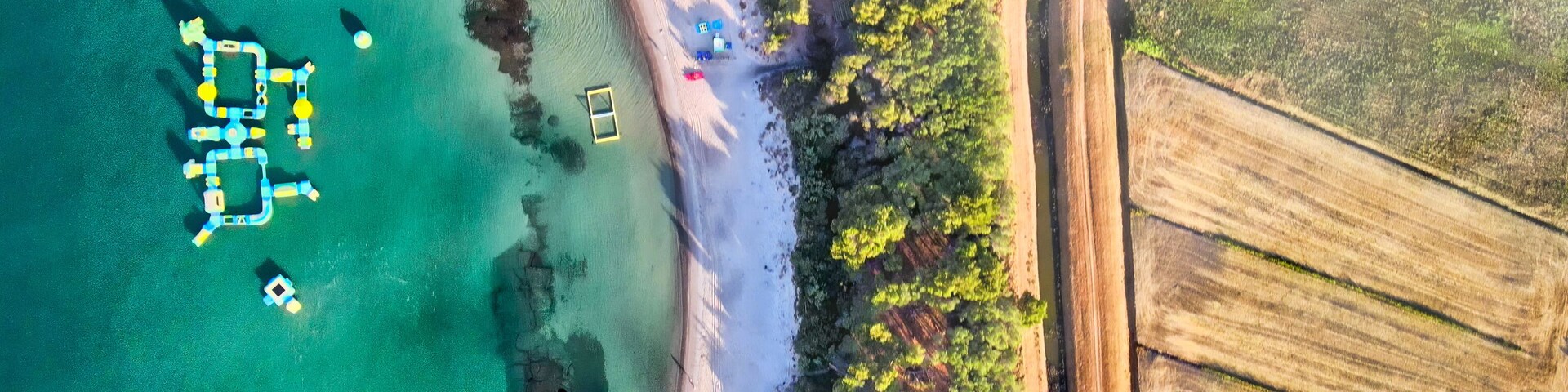 Vista aérea de una zona costera con aguas turquesas cristalinas, una playa de arena y un muelle con estructuras amarillas y azules.