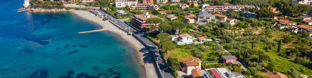 A coastal town with a clear blue sea, a beach, and residential buildings.
