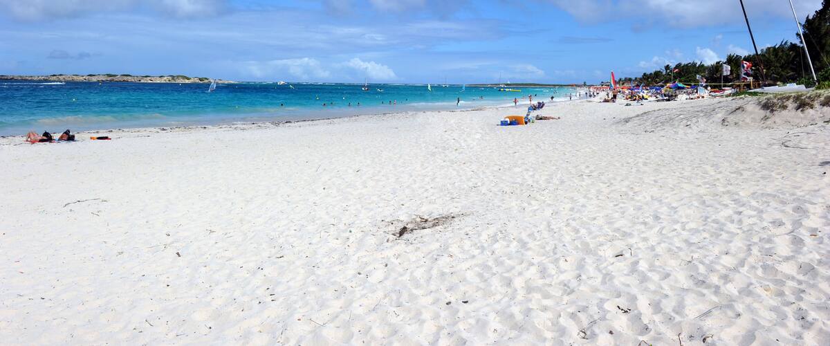 A sandy beach with clear blue water, a few boats, and umbrellas on the shore.