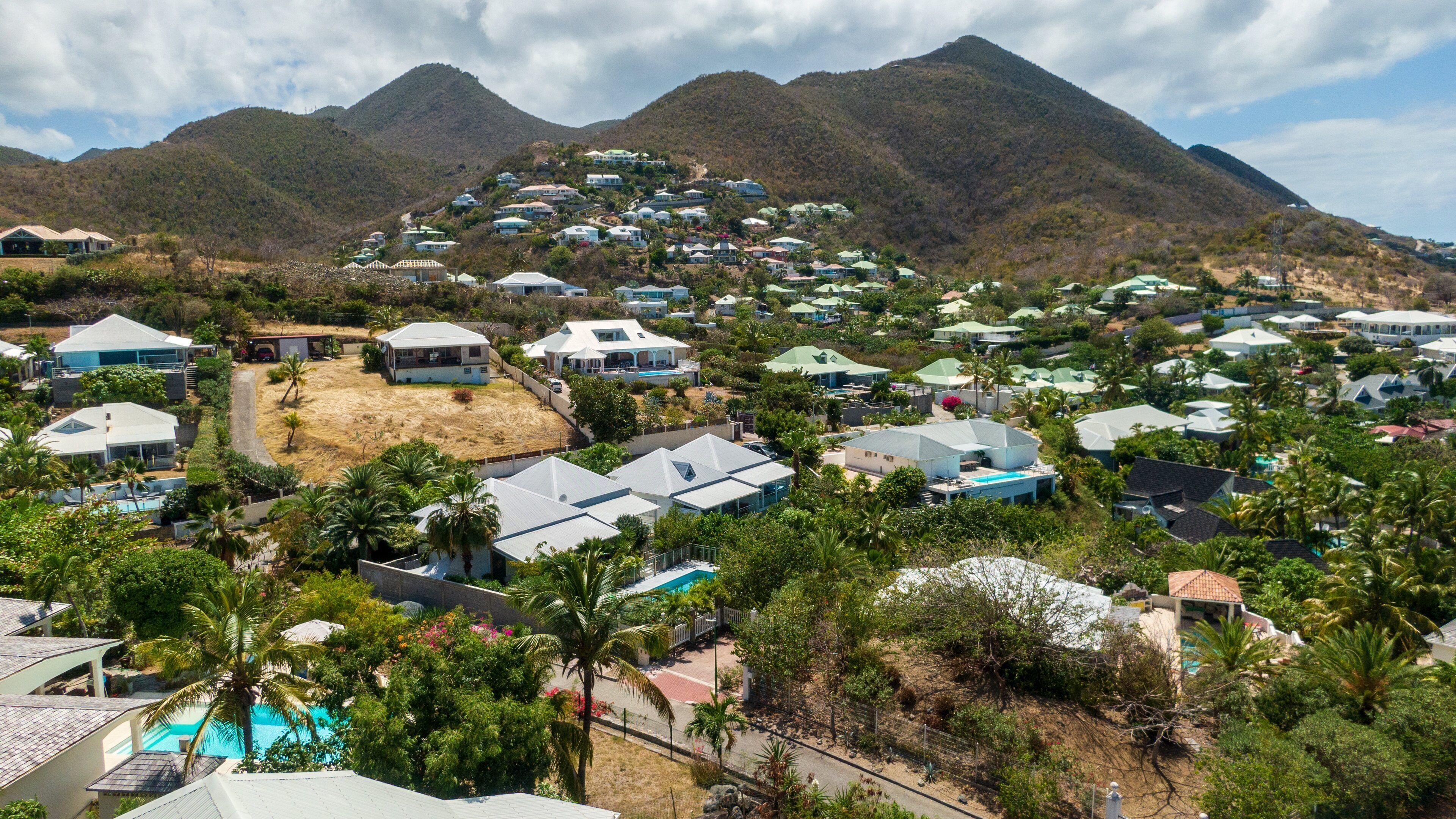 A hillside residential area with houses, a swimming pool, and mountains in the background.