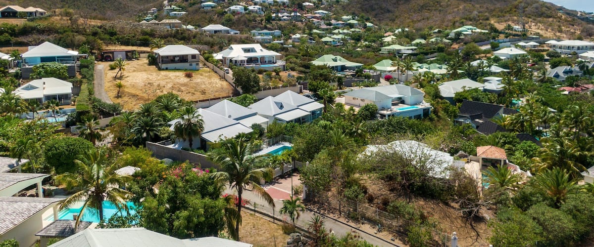 A hillside residential area with houses, a swimming pool, and mountains in the background.